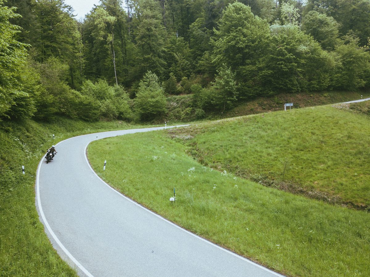 Kurvenstraße von oben mit Motorrad – Schweizer Jura
